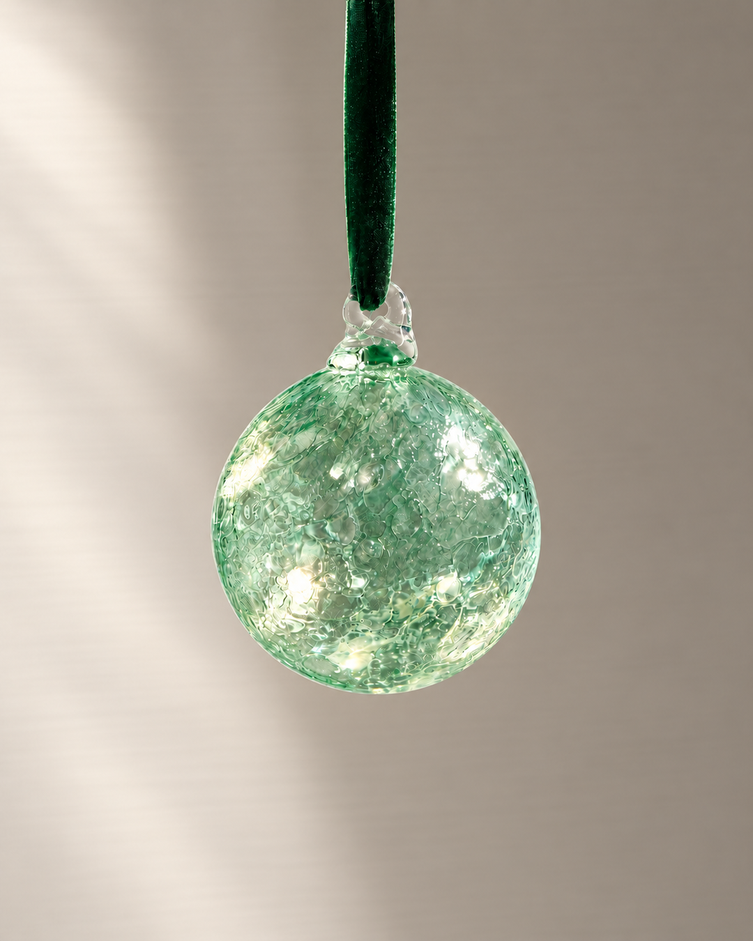 Green Lagoon Glass Bauble hanging from a velvet ribbon