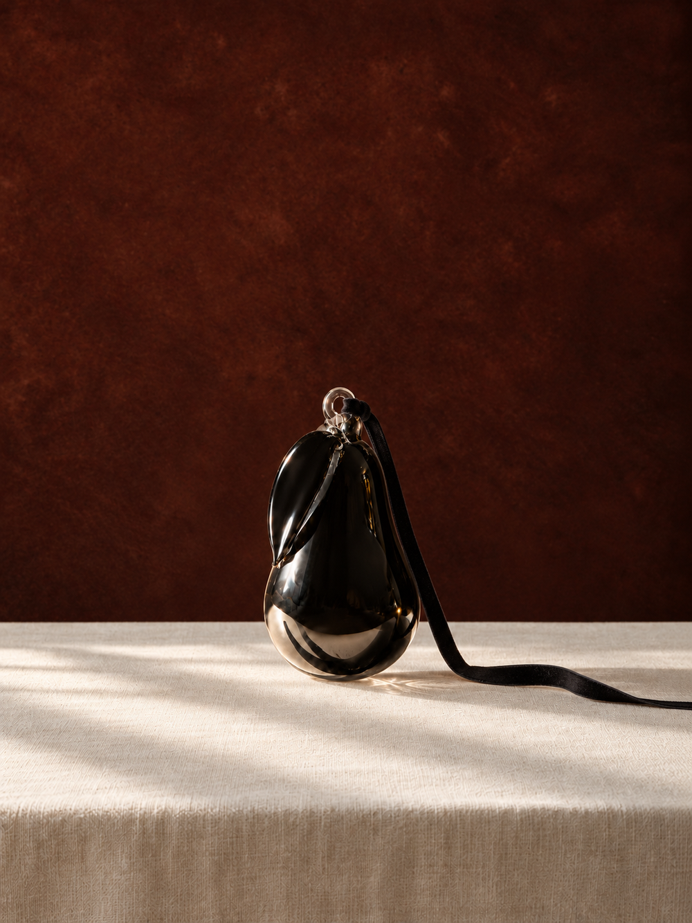 Smoke Hanging Glass Pear standing on ivory linen against a dark backdrop